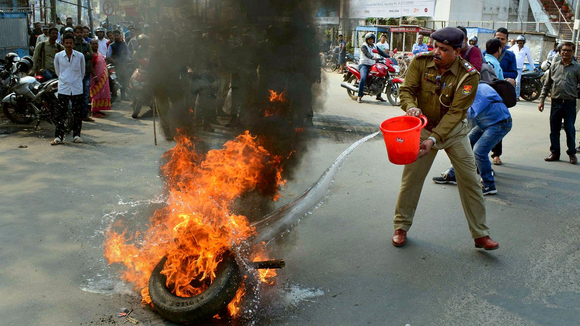 अगरतला में प्रदर्शनकारियों द्वारा सड़क पर जलाए गए टायरों को बुझाता पुलिसकर्मी