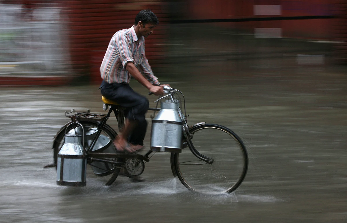 A man transporting empty milk cans rides his bicycle as it rains in Jammu. (Photo: Reuters)