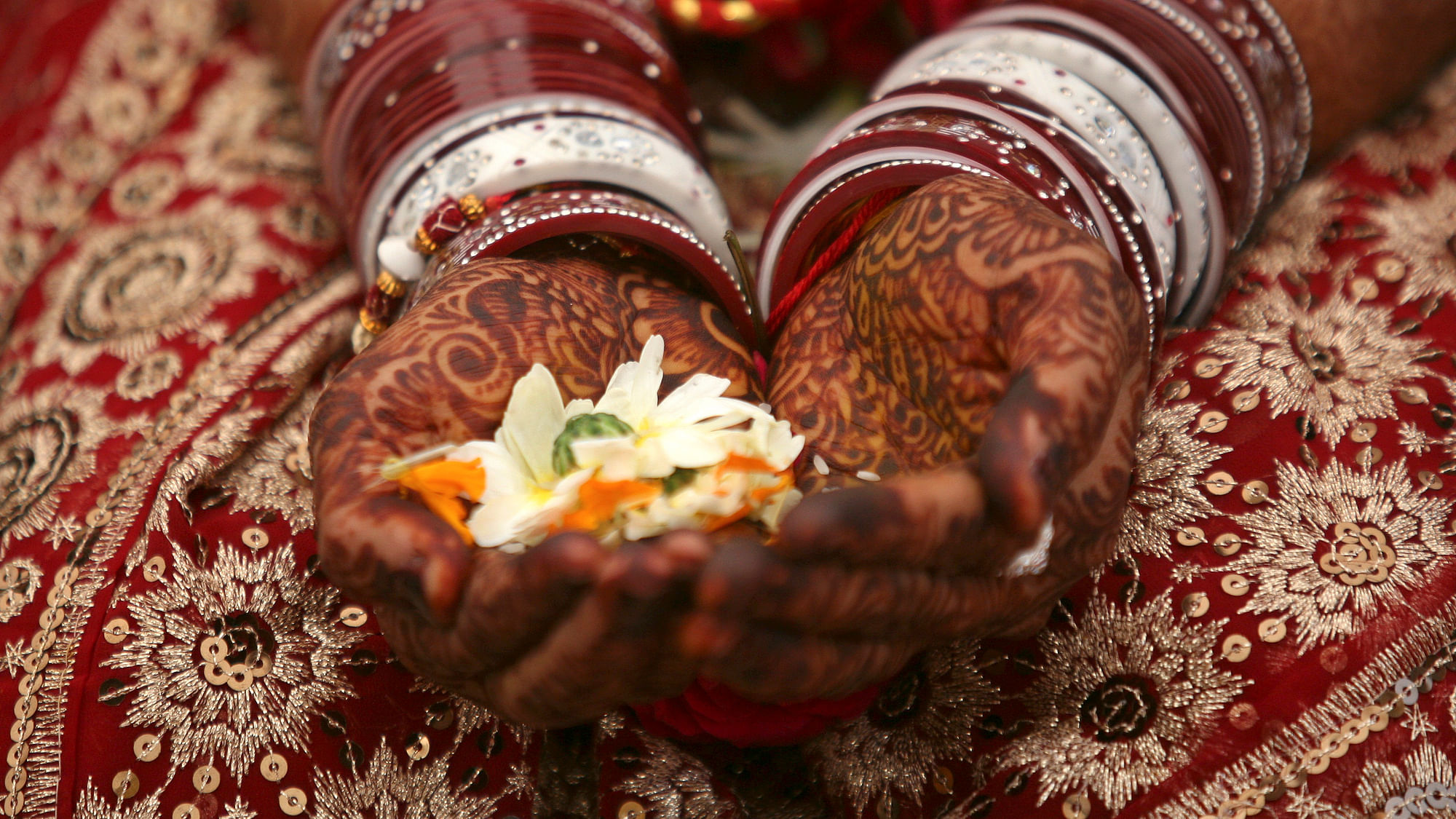 A bride holds flowers with her hands decorated with henna paste during her wedding ceremony
