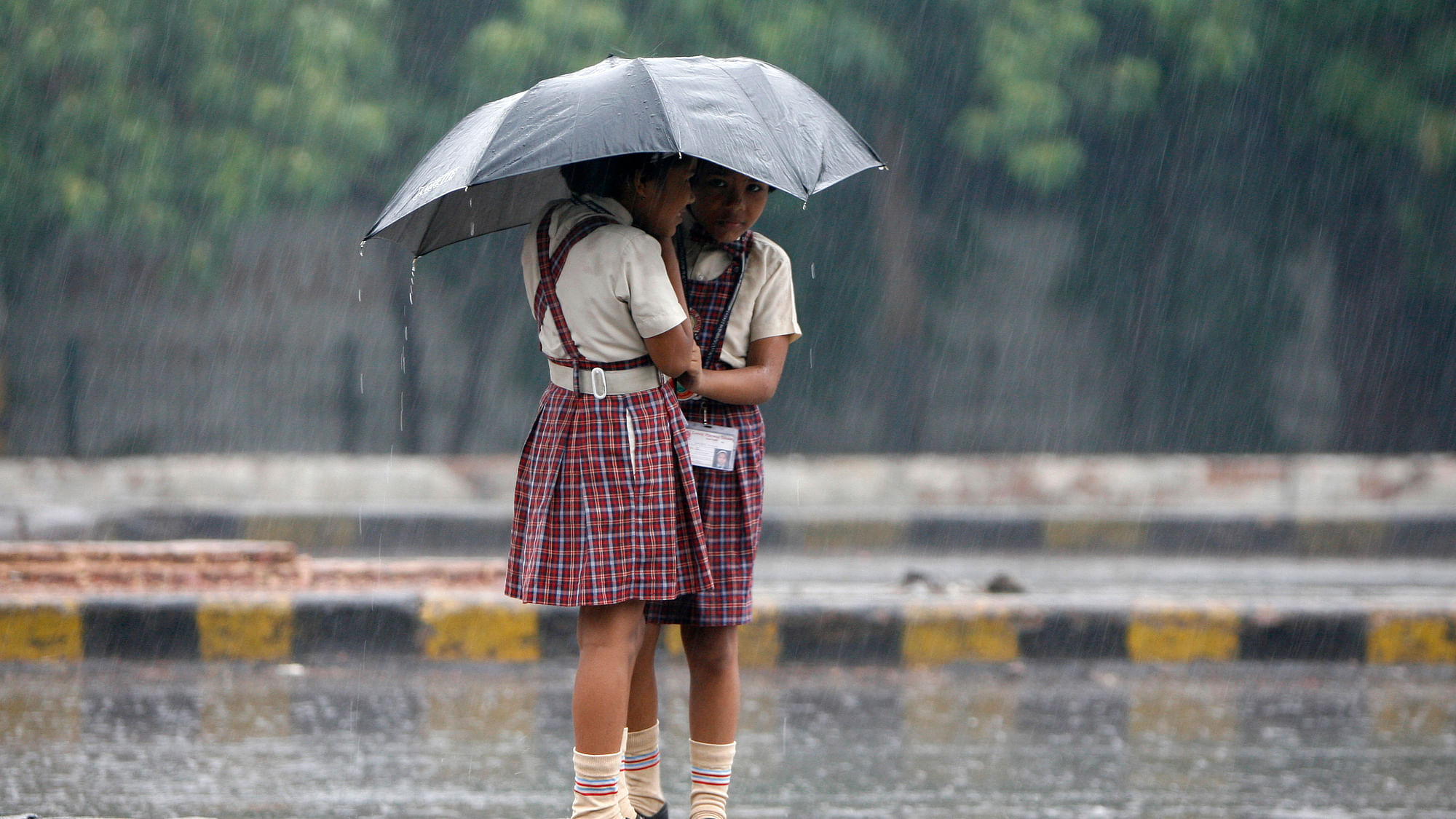 Schoolgirls stand on a road divider as they huddle under an umbrella during monsoon rains. Image used for representation.
