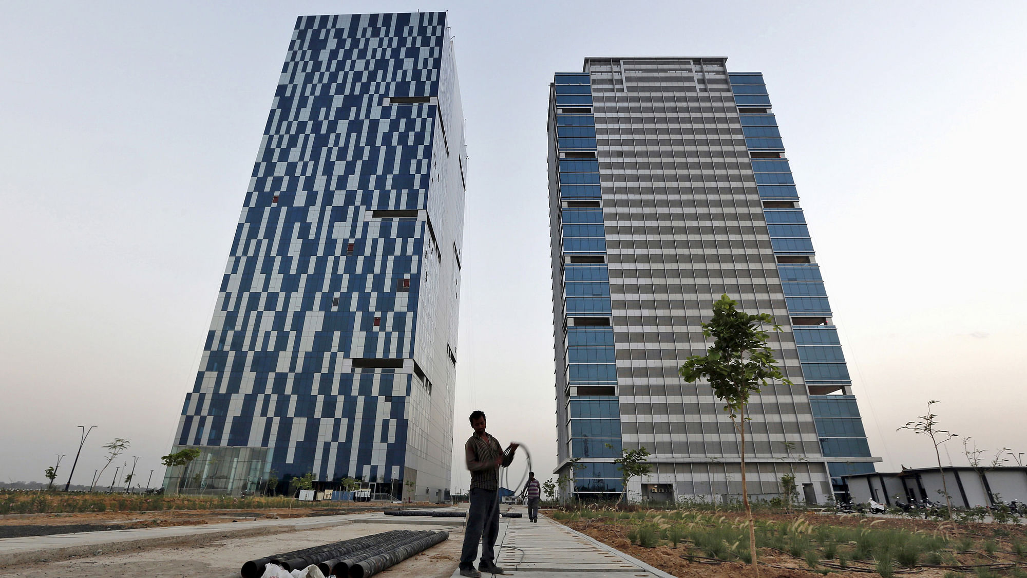 A worker folds the cable of a welding machine in front of two office buildings at the Gujarat International Finance Tec-City (GIFT) at Gandhinagar, in the western Indian state of Gujarat, April 10, 2015.