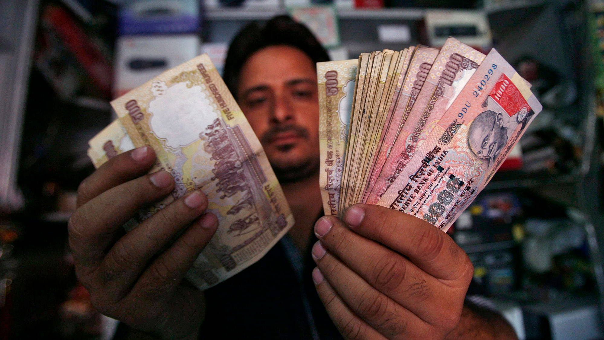 An Indian&nbsp;shopkeeper poses for a picture as he counts  notes at his shop. (Photo: Reuters)