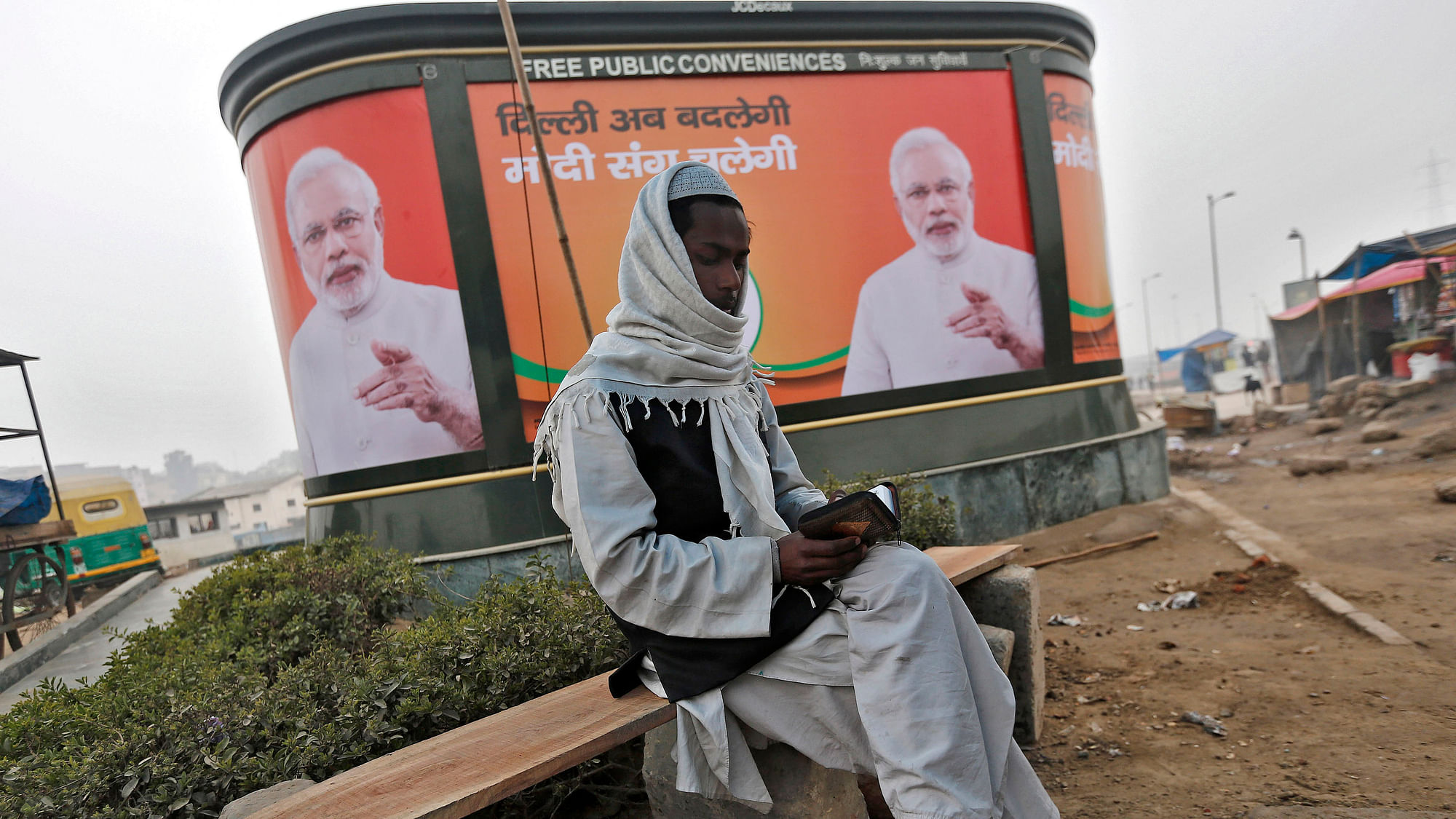 A Muslim man reads the Koran as he sits in front of a billboard featuring India’s Prime Minister Narendra Modi on a pavement along a road in New Delhi January 20, 2015. (Photo: Reuters)