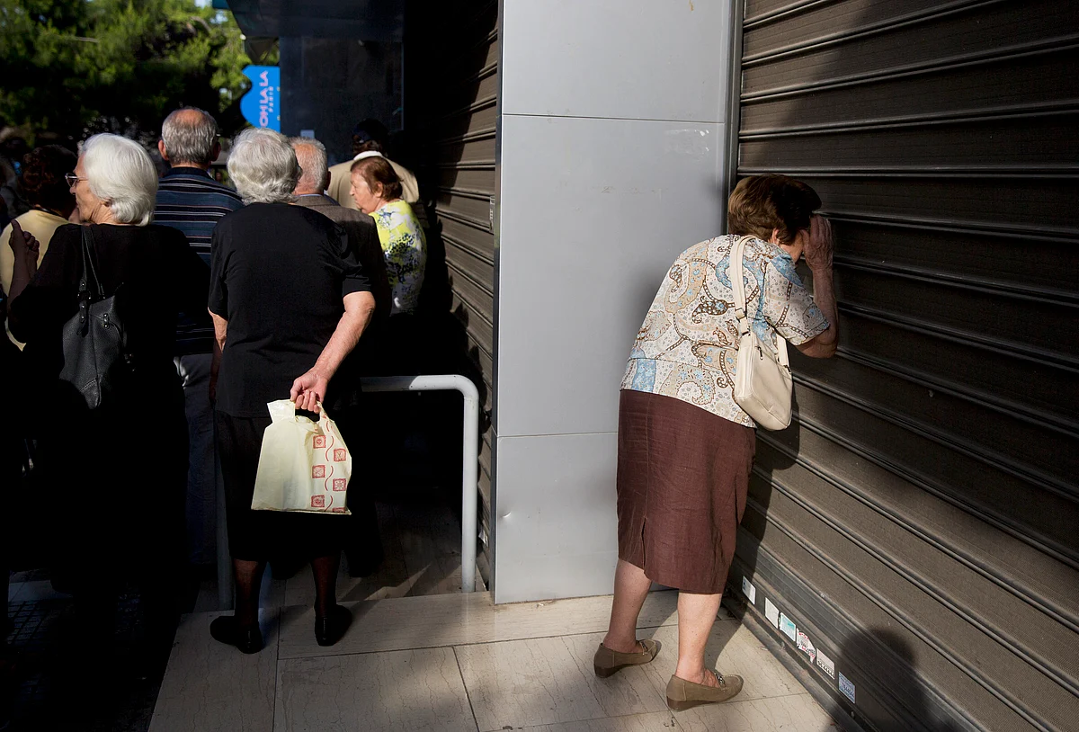 An elderly woman looks through the closed shutters of a bank as others, who usually get their pensions at the end of the month, wait outside a closed bank in Athens, Monday, June 29, 2015. (Photo: AP)