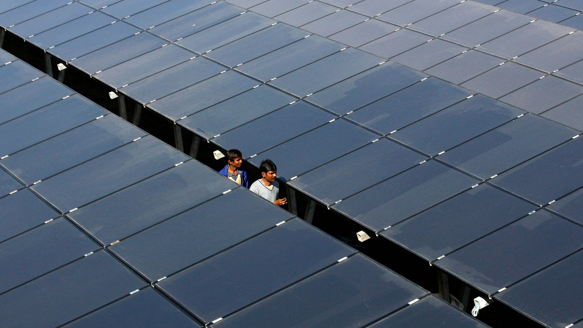Workers walk between rows of solar photovoltaics, inside a solar power plant at Raisan village near Gandhinagar. (Photo: Reuters)