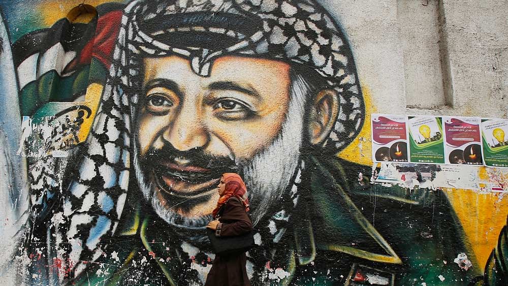 A Palestinian student walks past a mural depicting late Palestinian leader Yasser Arafat in Gaza City (Photo : Reuters)