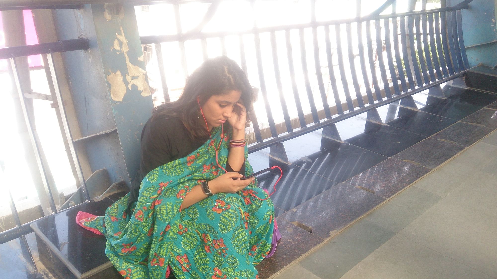 A passenger in the Delhi metro with earphones while waiting for her train. (Photo: The Quint)