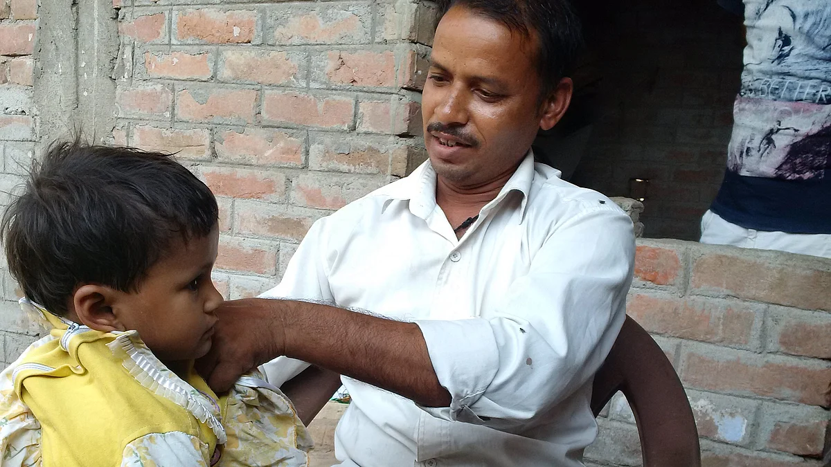 Ram Kumar, a Mahadalit from Mathura hamlet in Checher village, helping his daughter wear a frock. (Photo: <b>The Quint)</b>