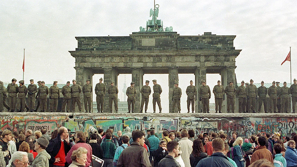 File photo of East Berlin border guards standing atop the Berlin Wall in front of the Brandeburg Gate on November 11, 1989. (Photo: Reuters)