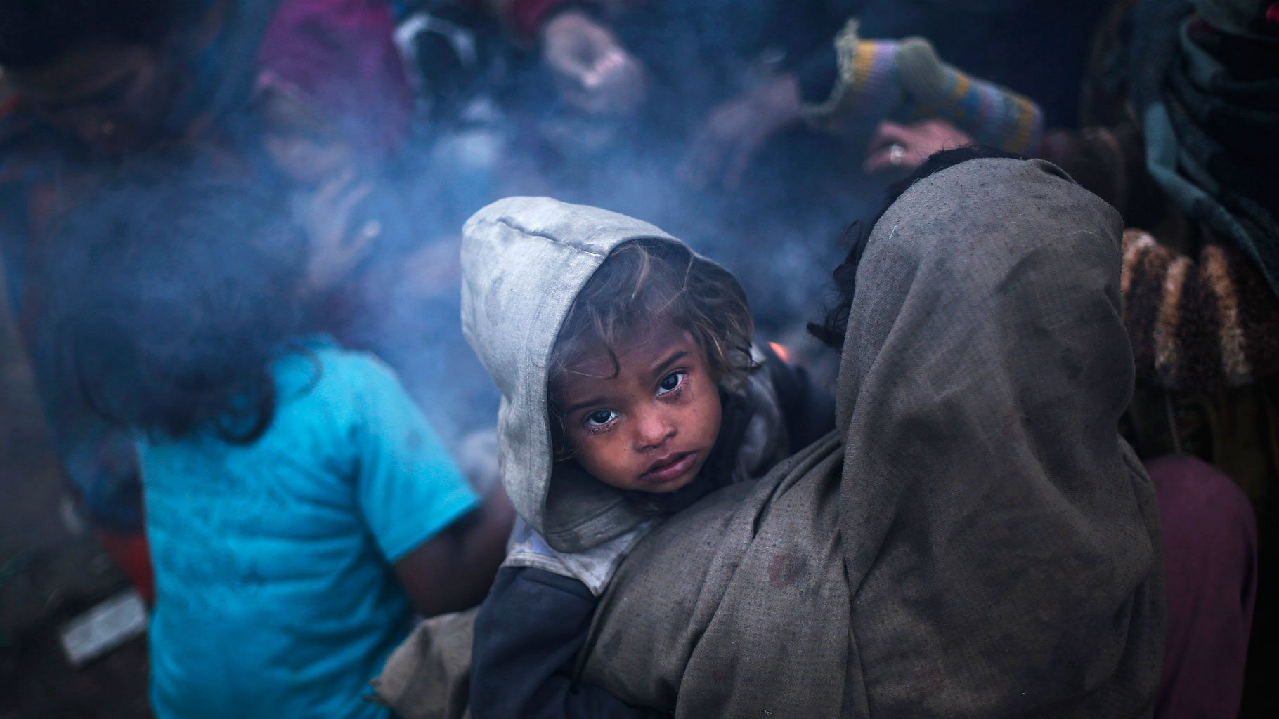 A woman holds her son as she sits with others next to a fire to warm themselves outside their temporary shelter on a cold winter morning in New Delhi December 25, 2014 (Photo: Reuters)