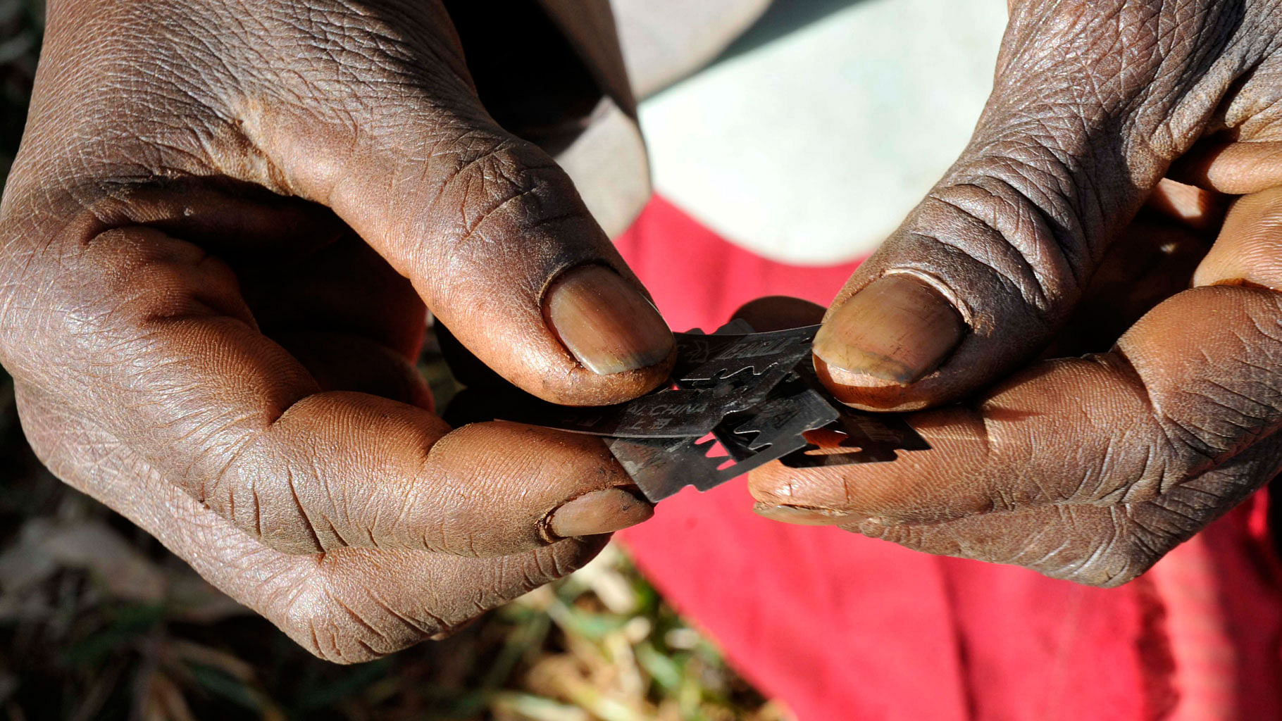 A traditional surgeon holds razor blades before carrying out female genital mutilation on teenage girls from the Sebei tribe in Uganda. (Photo: Reuters)