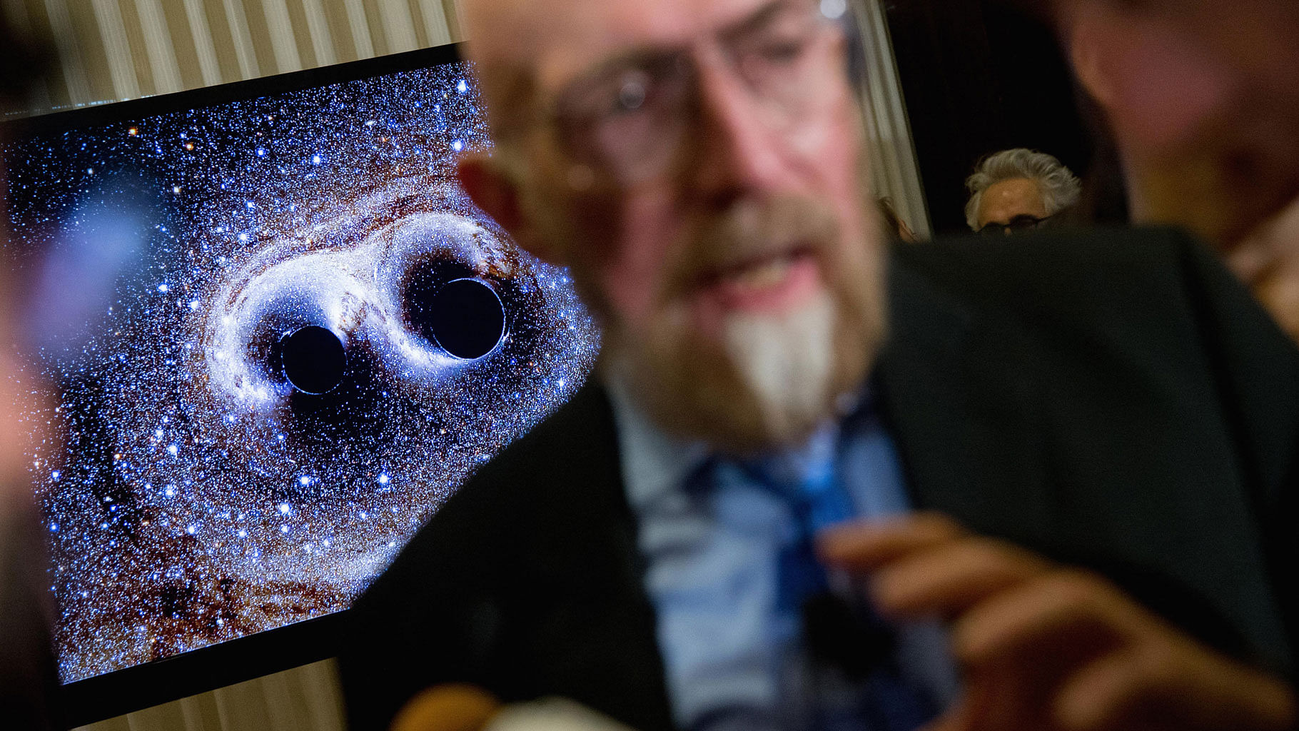 A visual of gravitational waves from two converging black holes is depicted on a monitor behind LIGO co-founder, Kip Thorne. (Photo: AP)
