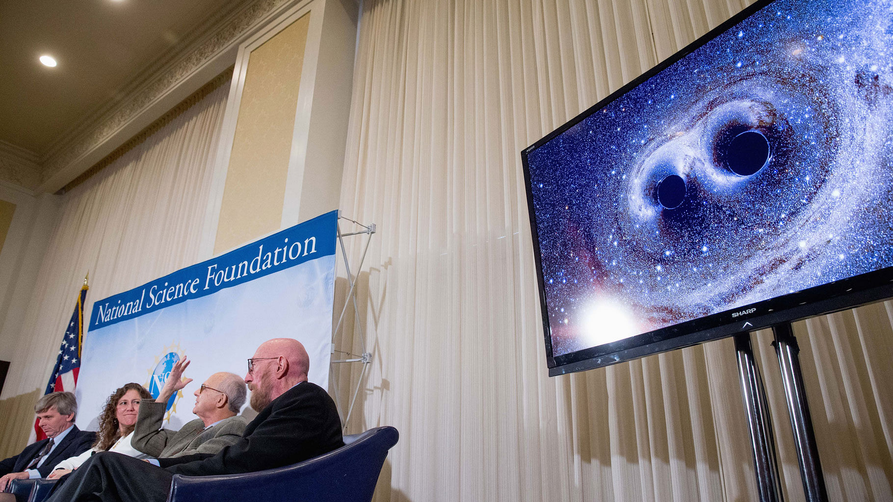 Scientists next to a visual of gravitational waves from two converging black holes. (Photo: AP)