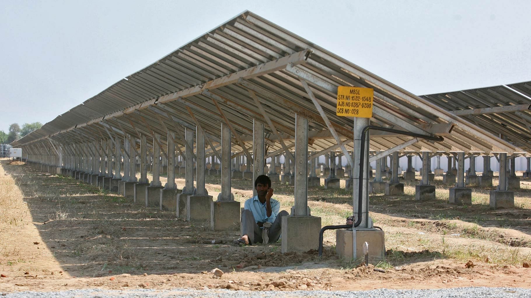 A worker speaks on a mobile phone as he sits under the installed solar panels of a newly inaugurated solar farm in Gujarat. (Photo: Reuters)