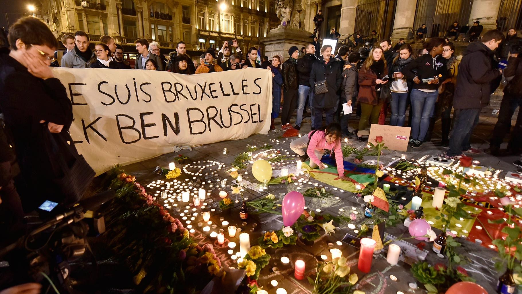 People holding a banner reading “I am Brussels” behind flowers and candles to mourn for the victims at Place de la Bourse in the center of Brussels, Tuesday, on 22 March, 2016. (Photo: AP)