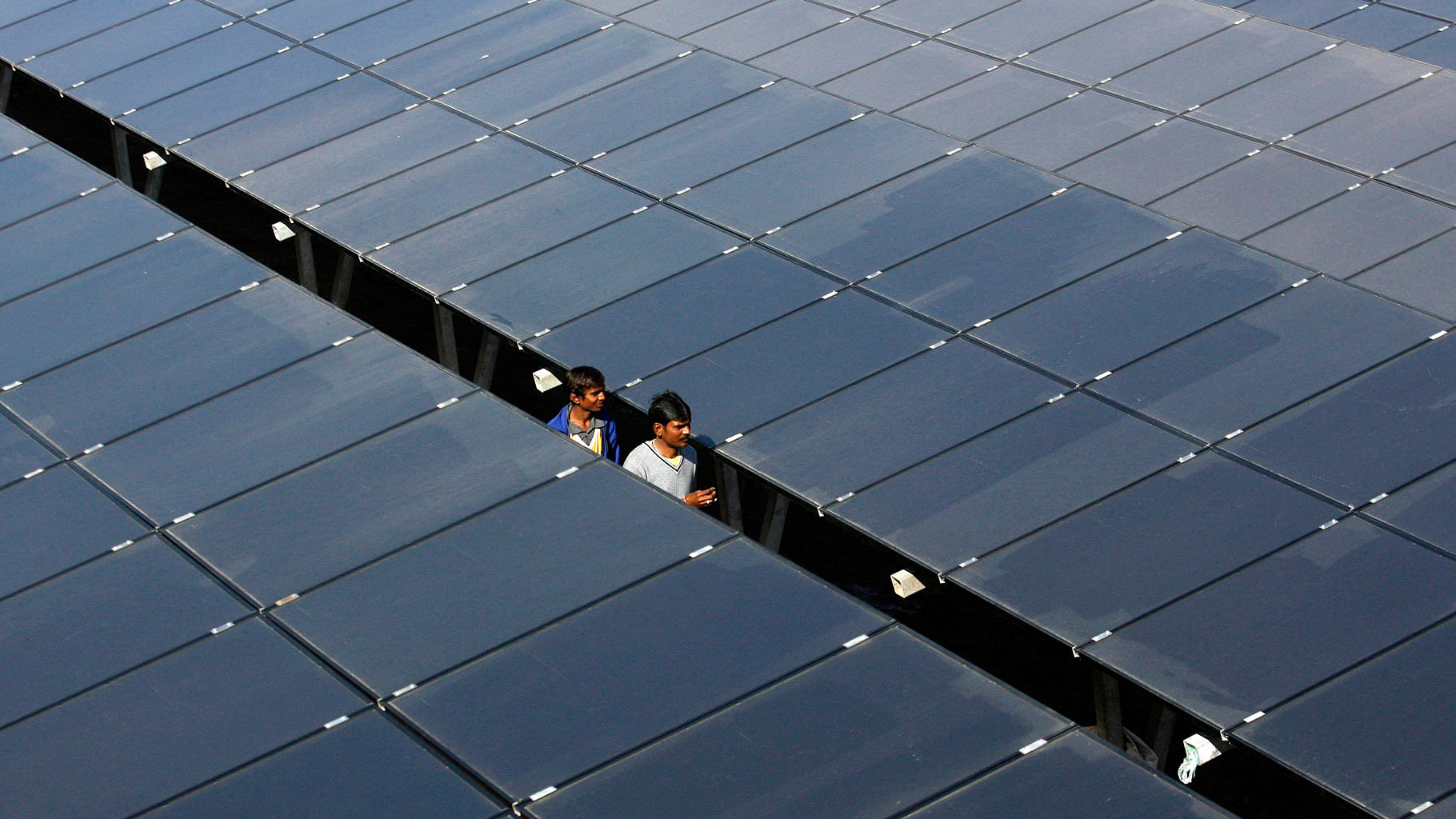 Workers walk in between rows of solar photovoltaics, inside a solar power plant at Raisan village near Gandhinagar. (Photo: Reuters)