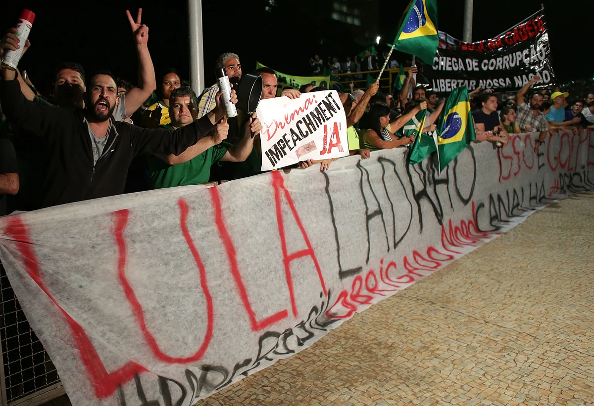 Demonstrators shout slogans from behind a banner that reads in Portuguese: “Lula thief”. (Photo: AP)