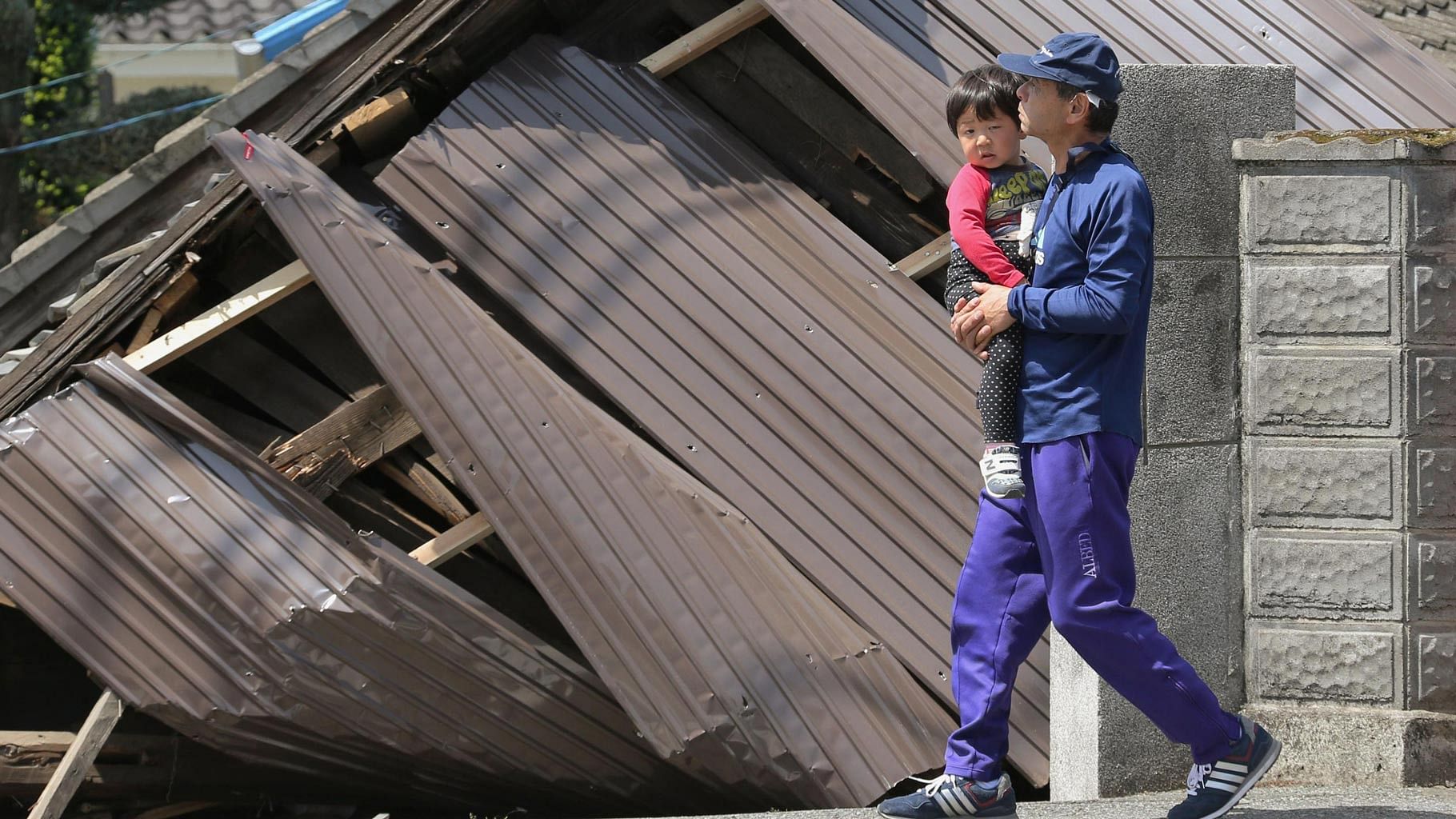 A man with a child, walks past houses destroyed by Thursday’s earthquake in Mashiki, Kumamoto. (Photo: AP)&nbsp;