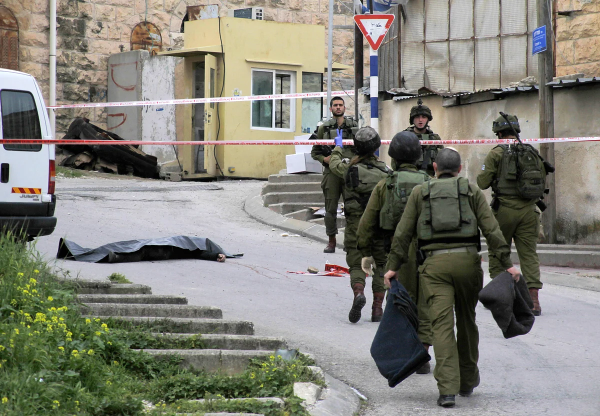In this Thursday, 24 March 2016 file photo, Israeli soldiers stand near the body of a Palestinian who was shot and killed by a soldier while laying wounded on the ground after a stabbing attack in Hebron, West Bank. (Photo: AP)