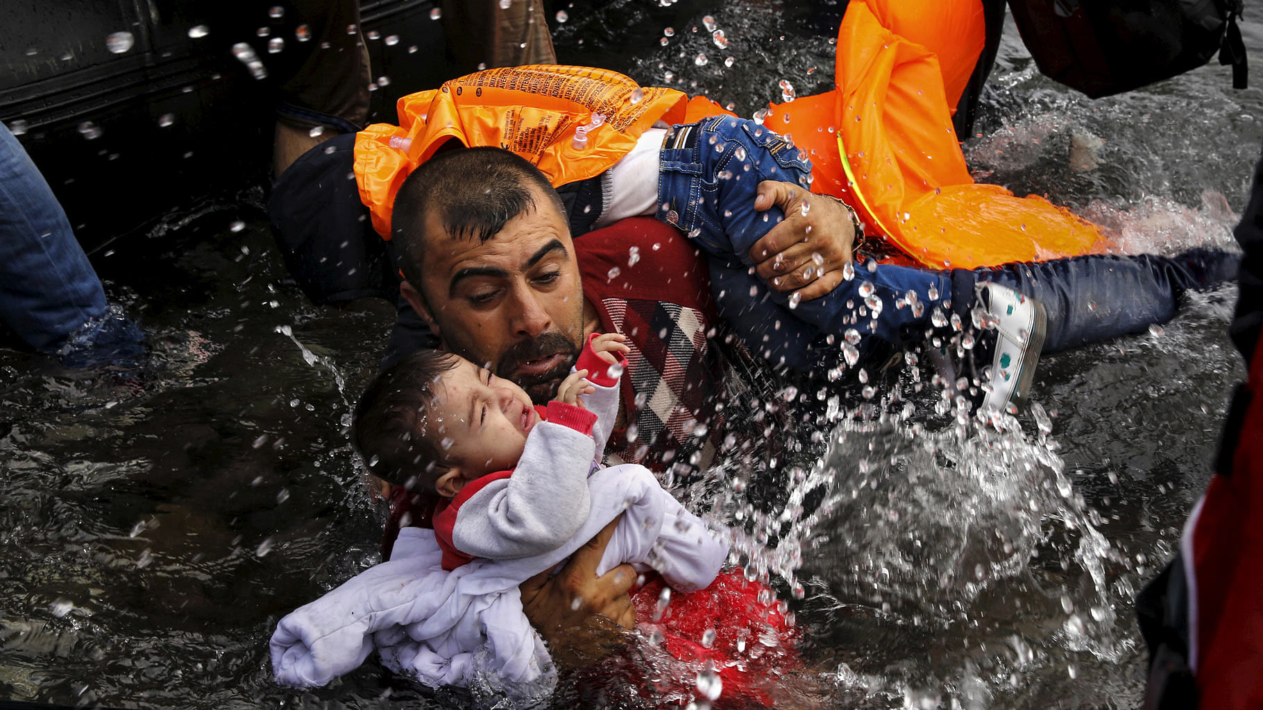 A Syrian refugee holds onto his children as he struggles to walk off a dinghy on the Greek island of Lesbos, after crossing a part of the Aegean Sea from Turkey to Lesbos 24 September  2015. (Photo: Reuters/Yannis Behrakis)