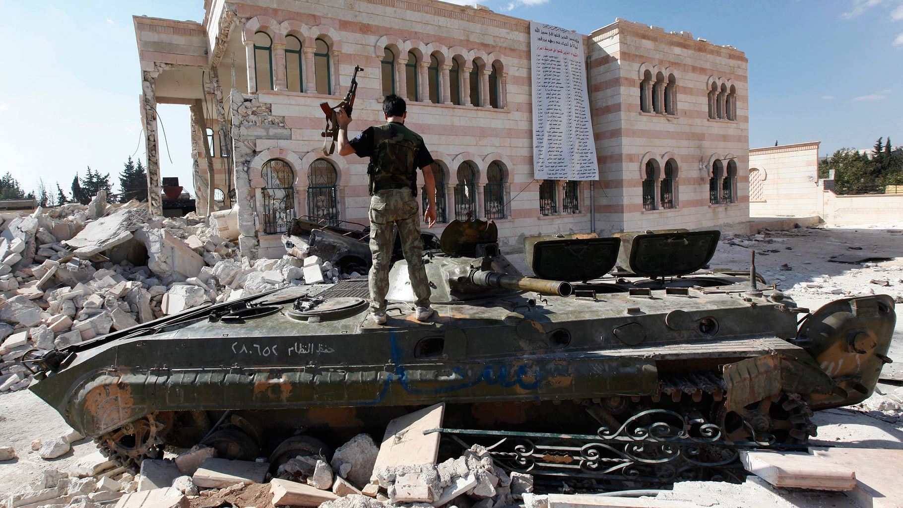 

Free Syrian Army soldier stands on a damaged Syrian military tank in front of a damaged mosque on the outskirts of Aleppo. (Photo: AP)