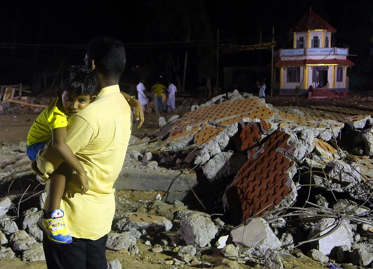 A man holds his child at the site of blast in Paravoor village, Kollam district, southern Kerala state, India, Sunday, 10 April 2016. (Photo: AP)