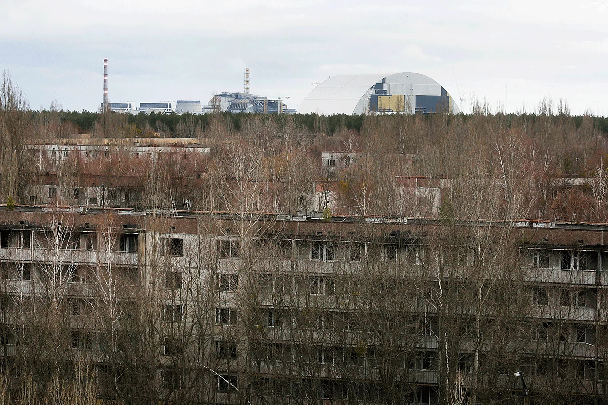 Trees grow into and onto derelict apartments in Pripyat, as the damaged reactor stands in the background, with the under-construction containment shield. (Photo: AP)