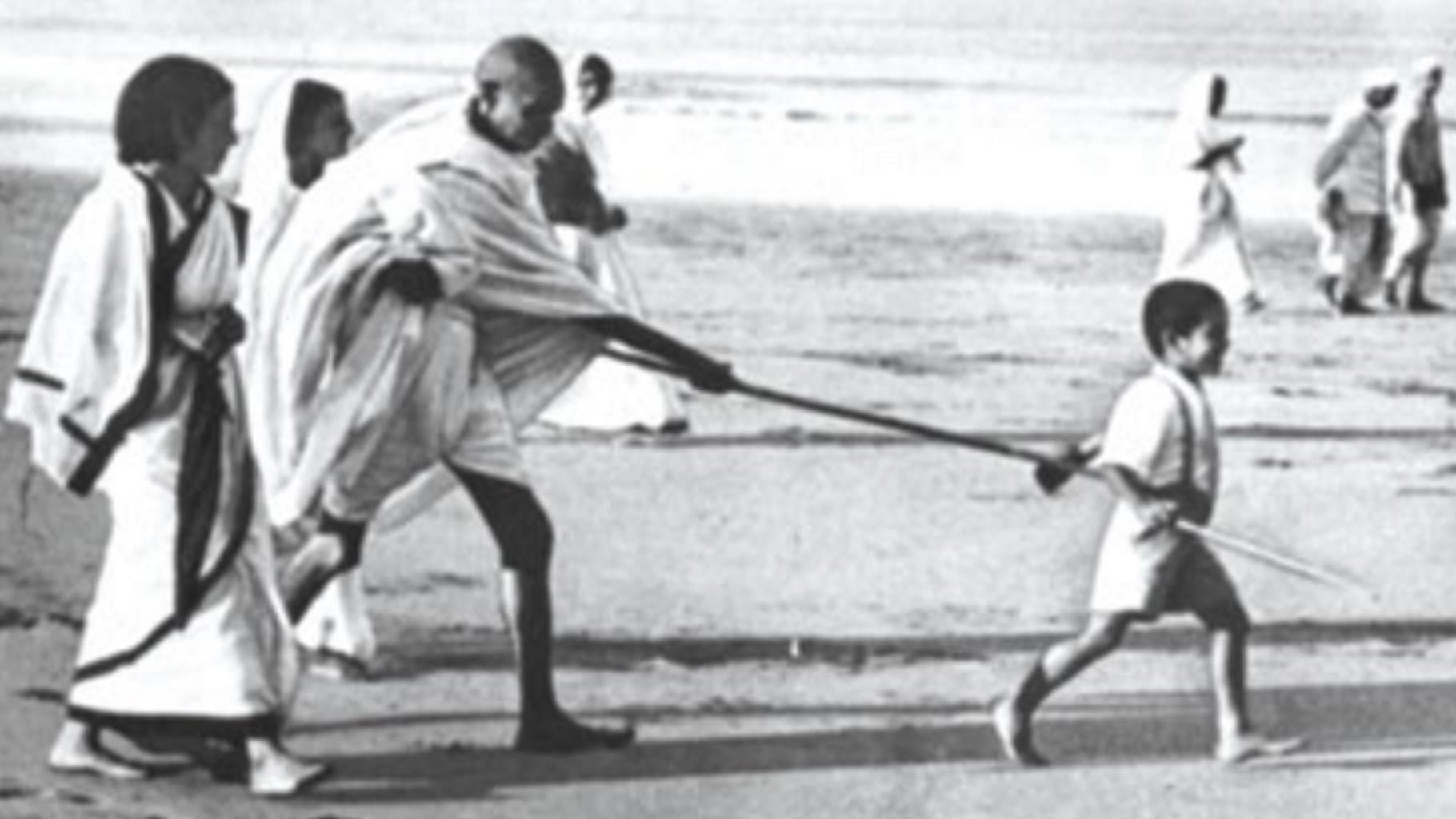 File photo of Kanubhai Gandhi pulling Mahatma Gandhi’s stick during a walk on a beach. (Photo Courtesy: <i><a href="http://www.universityexpress.co.in/delhiuniversity/2015/10/5-lesser-known-facts-mahatma-gandhi/">University Express</a></i>)