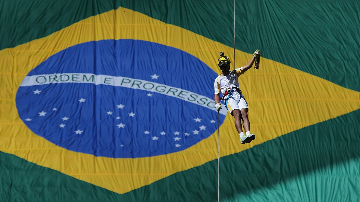 Brazil’s athlete Hudson Alves rappels down in front of a huge Brazilian flag, carrying the Olympic flame in a lantern during the torch relay in Brasilia. (Photo: AP)