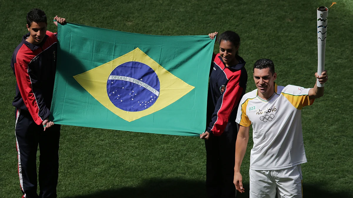 Brazil’s former soccer player Lucio da Silva Ferreira holds the Olympic torch by the Brazilian flag during the torch relay in Brasilia, Brazil. (Photo: AP)