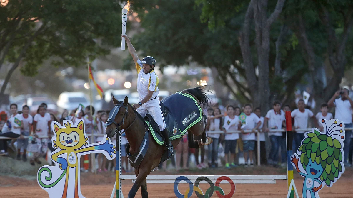 Jose Batista holds the Olympic torch aloft as he rides his horse over the obstacle course. (Photo: AP)