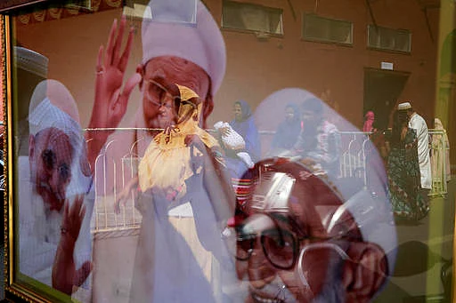 Indian Dawoodi Bohra women, scarves on their head, are reflected on a portrait showing three generations of Syednas, or religious head, in a Bohra neighborhood in Mumbai. (Photo Courtesy: AP Images)