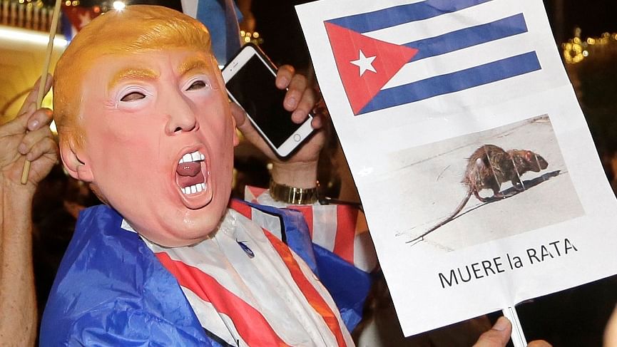 A person wearing a Donald Trump mask holds a sign in Spanish that reads the Rat Dies as he celebrates the death of Fidel Castro. (Photo: AP)
