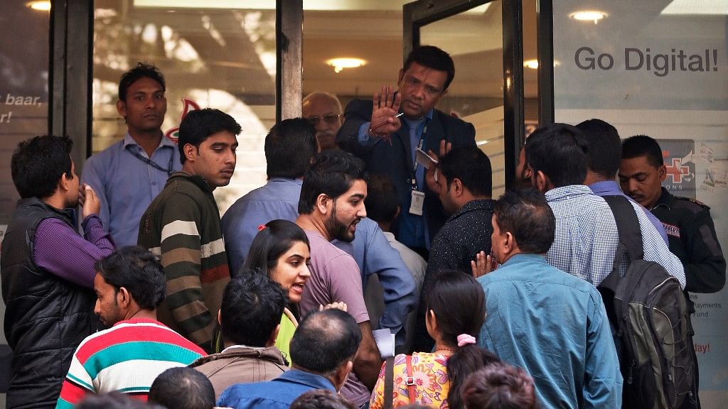 A bank official asks people to wait patiently in queues outside a bank in New Delhi. (Photo: AP)