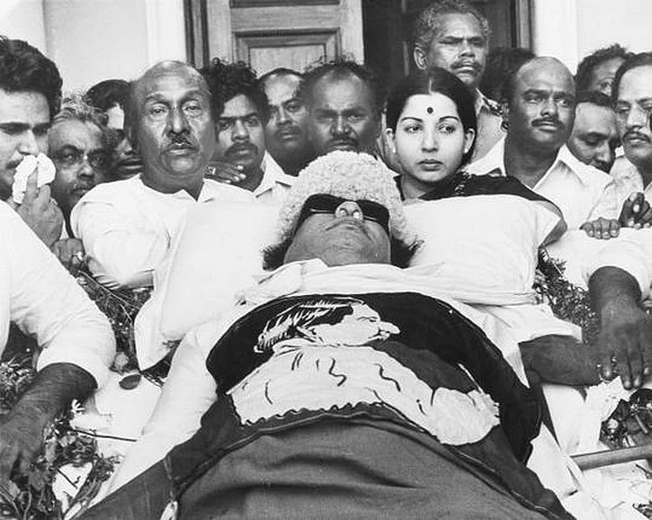 MGR’s body lies in state at Rajaji Hall in Chennai. Jayalalithaa can be seen standing beside his body. (Photo: <a href="http://MGR’s body lies in state at Rajaji Hall in Chennai. Jayalalithaa can be seen standing beside his body. (Photo: kmhouseindia Blogspot)">kmhouseindia blogspot</a>)