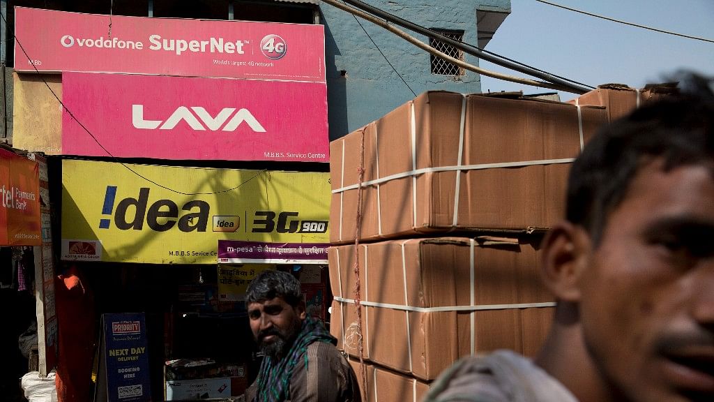 Workers walk past an advertisement of Idea Cellular and Vodafone in New Delhi. (Photo Courtesy: AP)