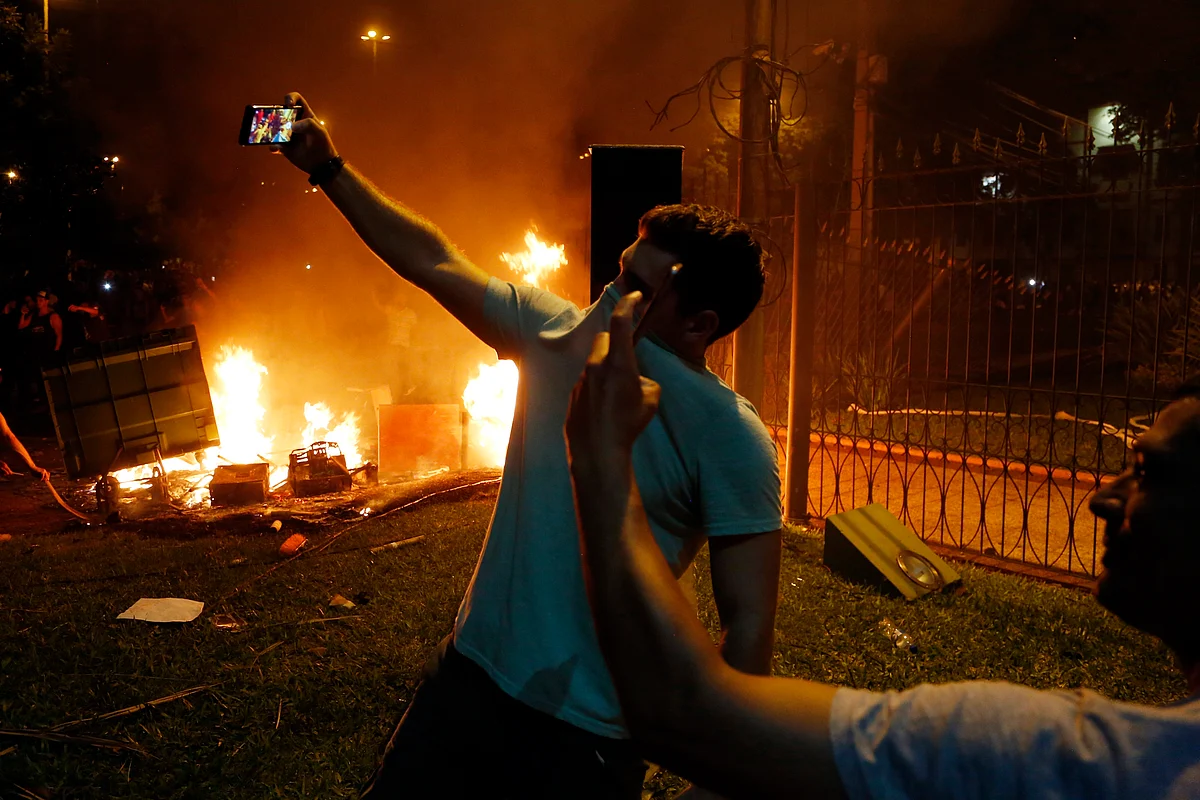 Two men pose for “selfies” during the protest against presidential re-elections at Congress in Asuncion. The protesters set ablaze the first floor of the Congress. (Photo: AP)