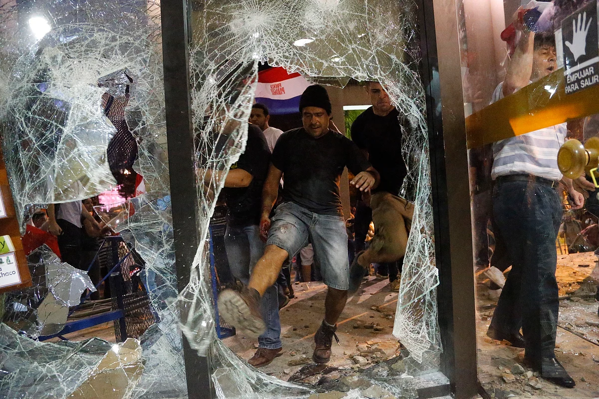 A man kicks at a shattered window of the congress building during clashes between police and protesters. Police used water cannon and fired rubber bullets to drive demonstrators away from the building while firefighters extinguished blazes inside. (Photo:AP)