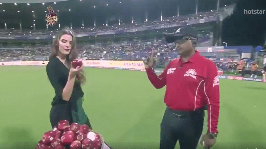 A model asks an IPL umpire to choose between apples and the ball before a match. (Photo: Twitter)