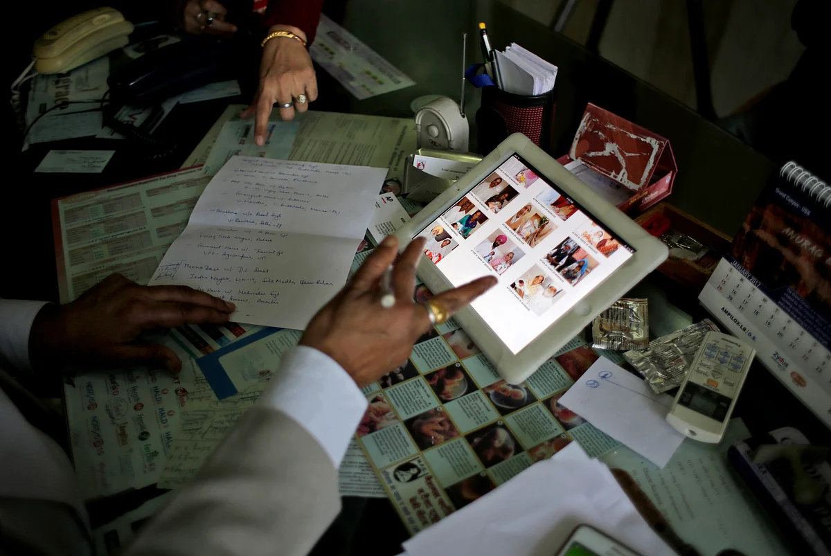 Dr Anurag Bishnoi, bottom, browses through photographs of his patients on his iPad in his office at the National Fertility and Test Tube Baby Centre in Hisar. The packed waiting room at Bishnoi’s clinic bears witness to the fact that working-class families across the country are willing to spend their limited savings for a child of their own. (Photo: AP)