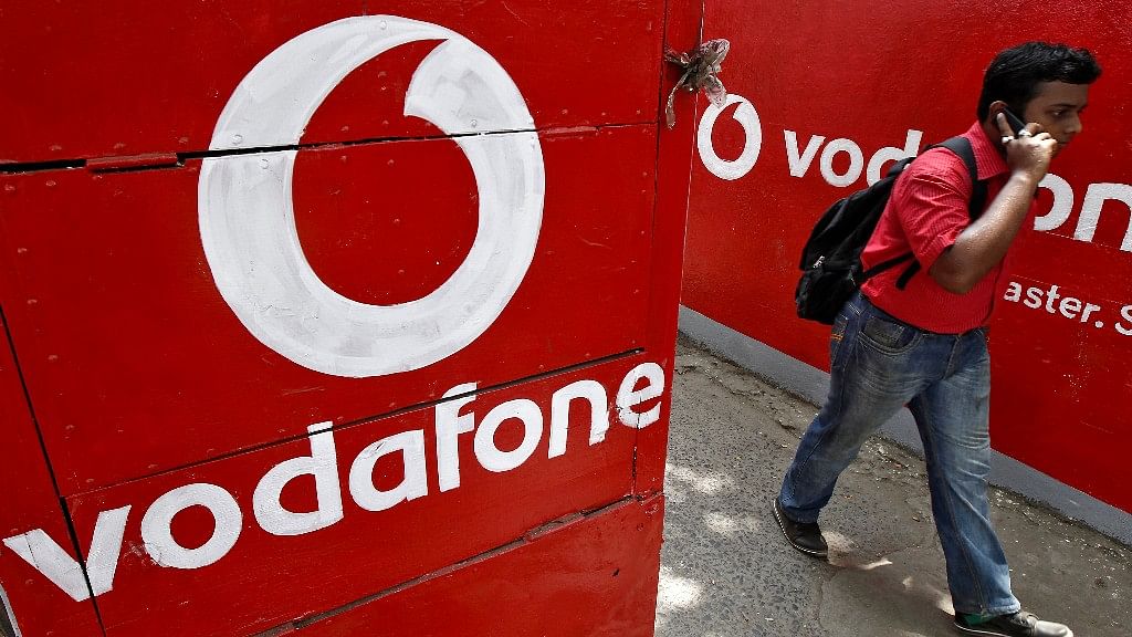 A man speaks on his mobile phone as he walks past logos of Vodafone painted on a roadside wall in Kolkata (Photo: Reuters)