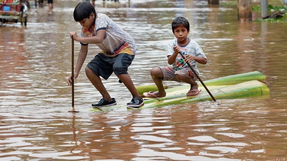 Two boys crossing a flooded street on a raft made of banana tree trunk in Assam.