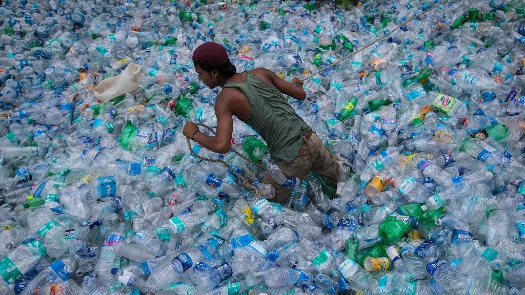Representational image of a worker  moving through a pile of empty plastic bottles at a recycling workshop. 