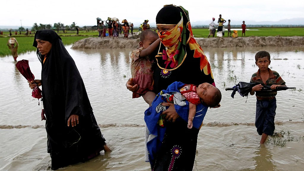 A Rohingya refugee woman carry children while walking in the water after travelling over the Bangladesh-Myanmar border in Teknaf, Bangladesh