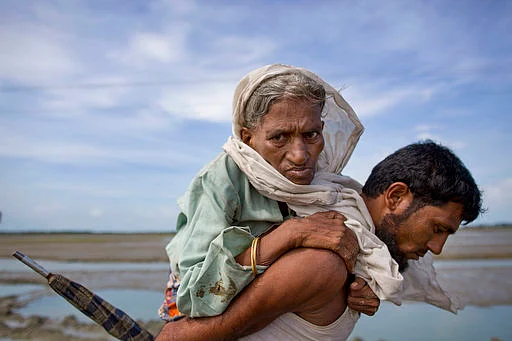 A Rohingya Muslim man carries an elderly woman and walks towards a camp for refugees after crossing over the border from Myanmar into Bangladesh in Teknaf, Bangladesh