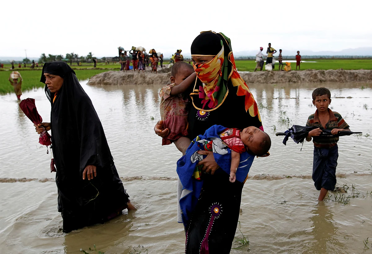A Rohingya refugee woman carry children while walking in the water after travelling over the Bangladesh-Myanmar border in Teknaf, Bangladesh.