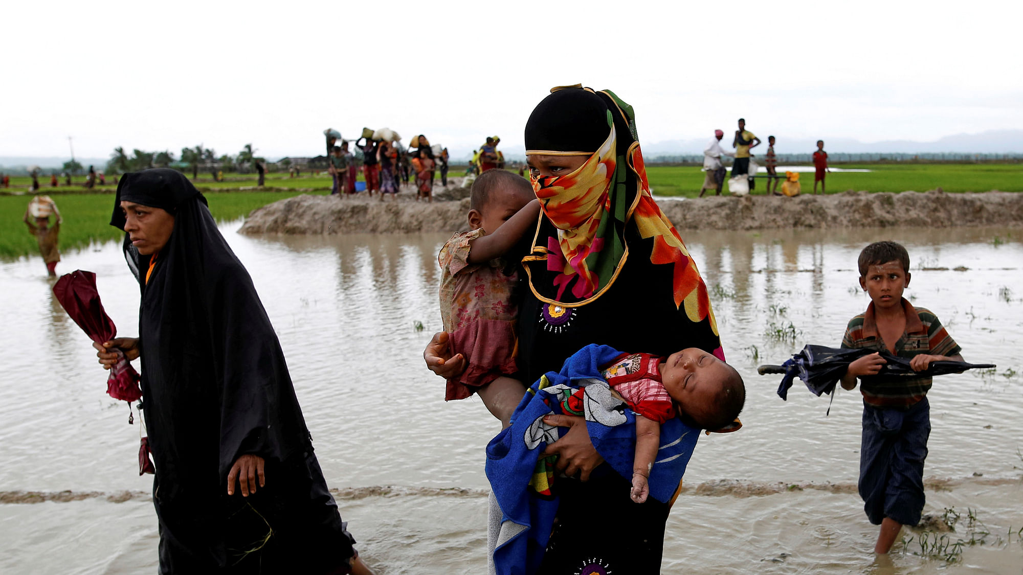 A Rohingya refugee woman carry children while walking in the water after travelling over the Bangladesh-Myanmar border in Teknaf, Bangladesh.