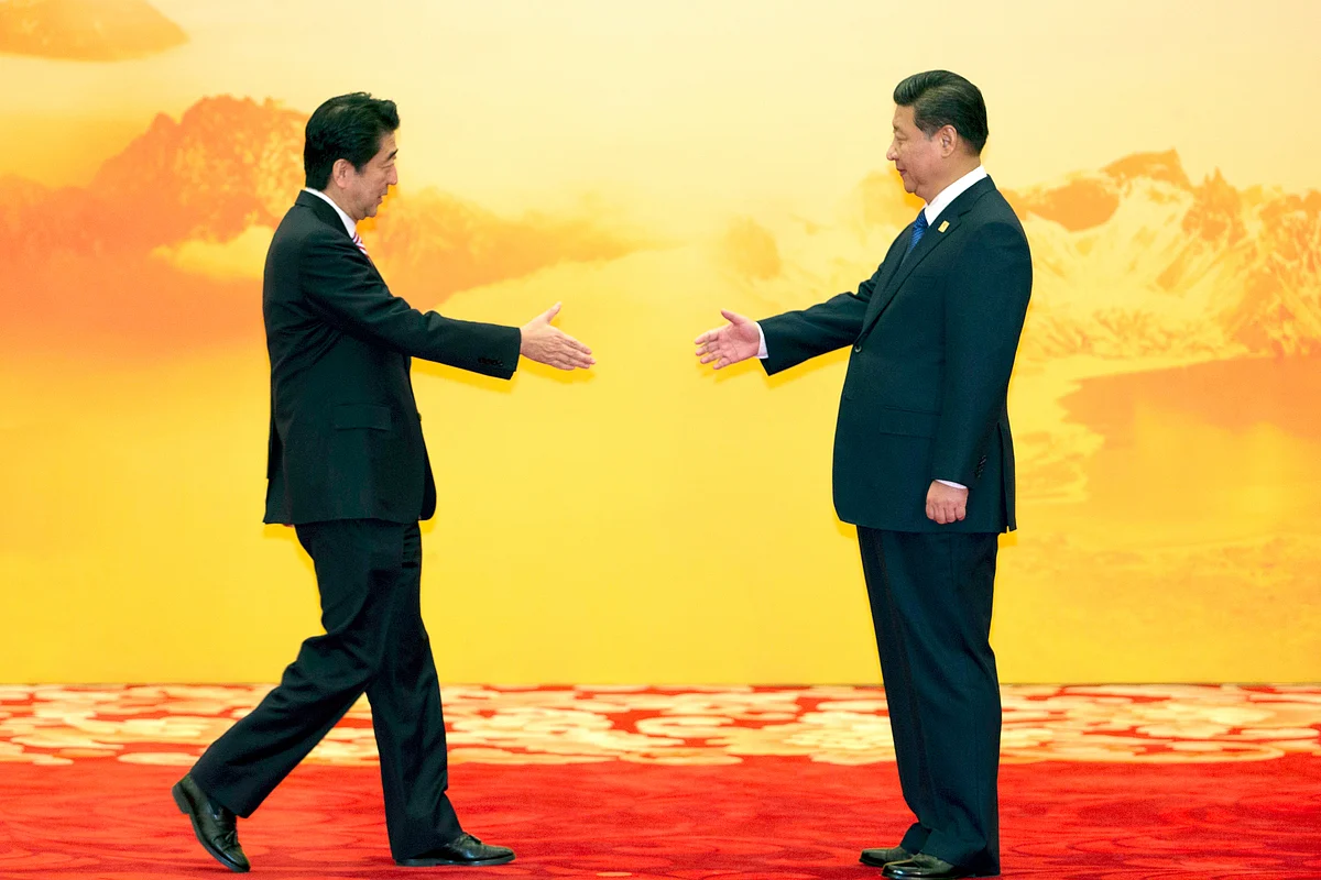 In this 11 November 2014 file photo, Japan’s Prime Minister Shinzo Abe reaches out to shake hands with Chinese President Xi Jinping during a regional economic meeting in Yanqi Lake, Beijing.