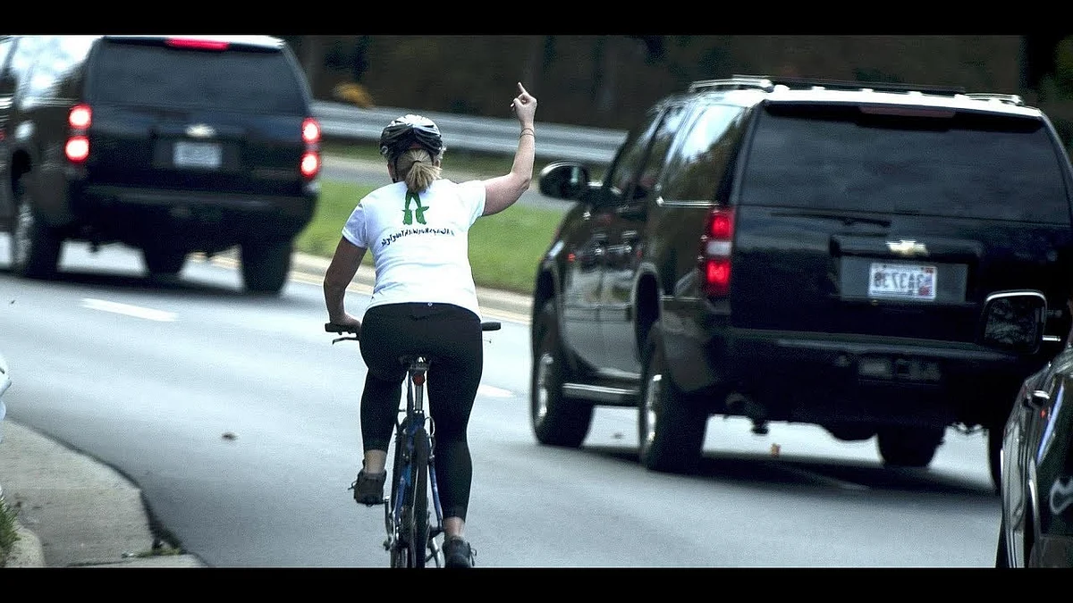 Cycling woman shows Trump he finger as his car drives by her.