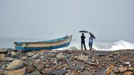 A couple of fishermen using umbrellas to protect themselves from rough weather under the influence of Ockhi.